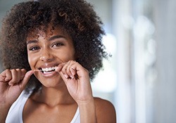 Woman flossing to prevent dental emergencies in Fort Worth