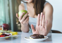 Woman pushing donut away while holding an apple