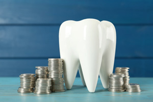 Large model tooth on blue surface surrounded by stacks of shiny coins