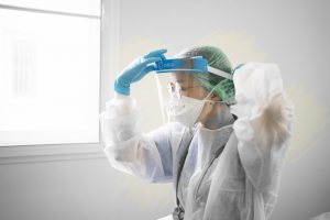 dentist wearing surgical gown, hair covering, gloves, mask, and face shield