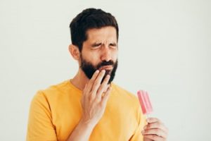 Man holding his mouth in pain and holding a popsicle in his other hand