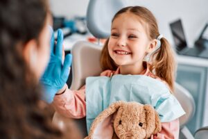 Girl with pigtails holding stuffed bunny sitting in dentist chair high fiving the dentist